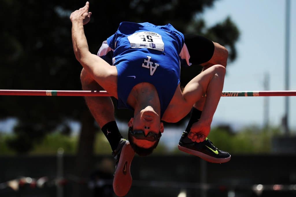 man jumping over red rod