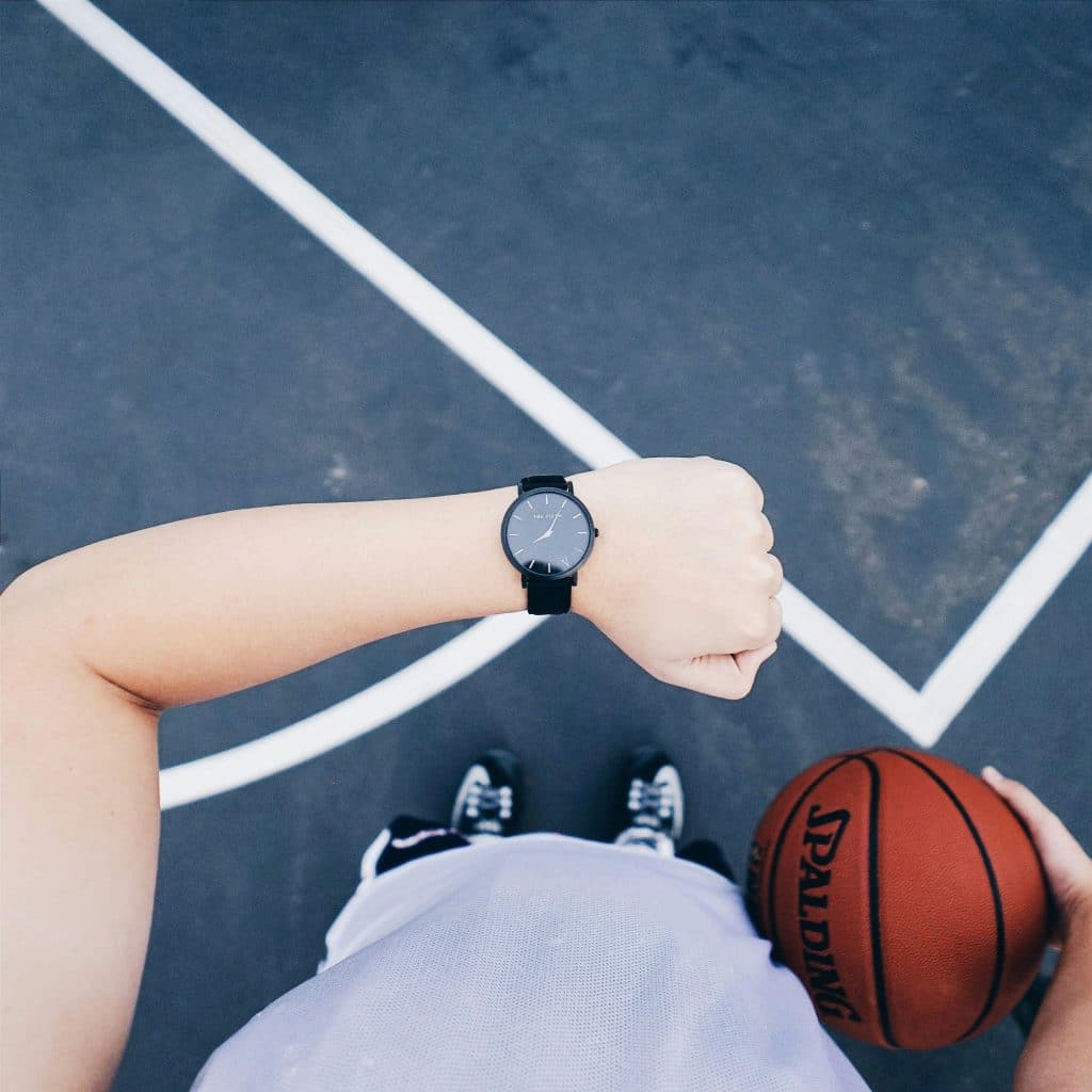 Person wearing black round analog watch on left wrist while holding basketball on right hand